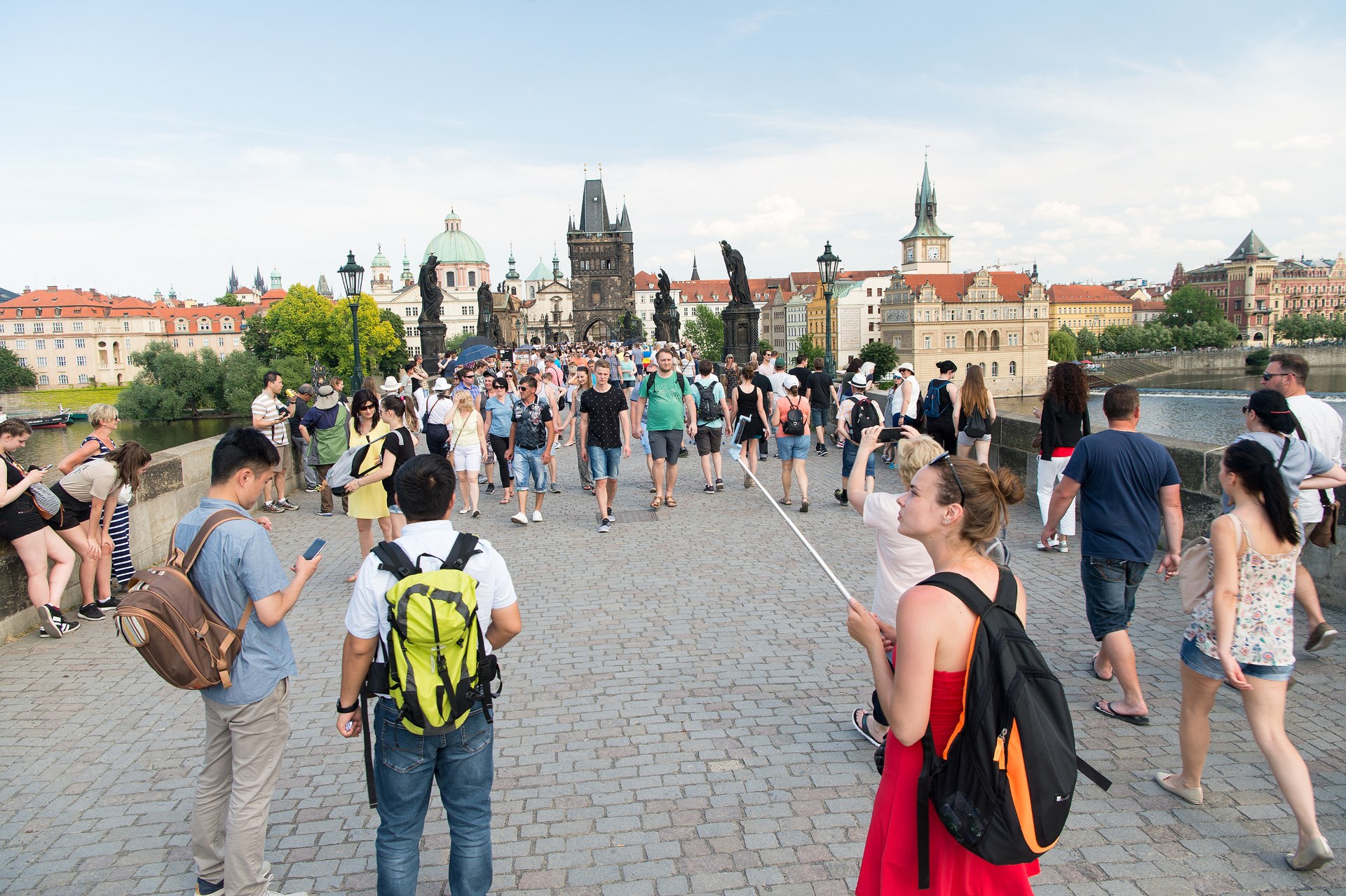 Młodzi ludzie z plecakami na Moście Karola w Pradze, w tle wieża mostowa Starego Miasta