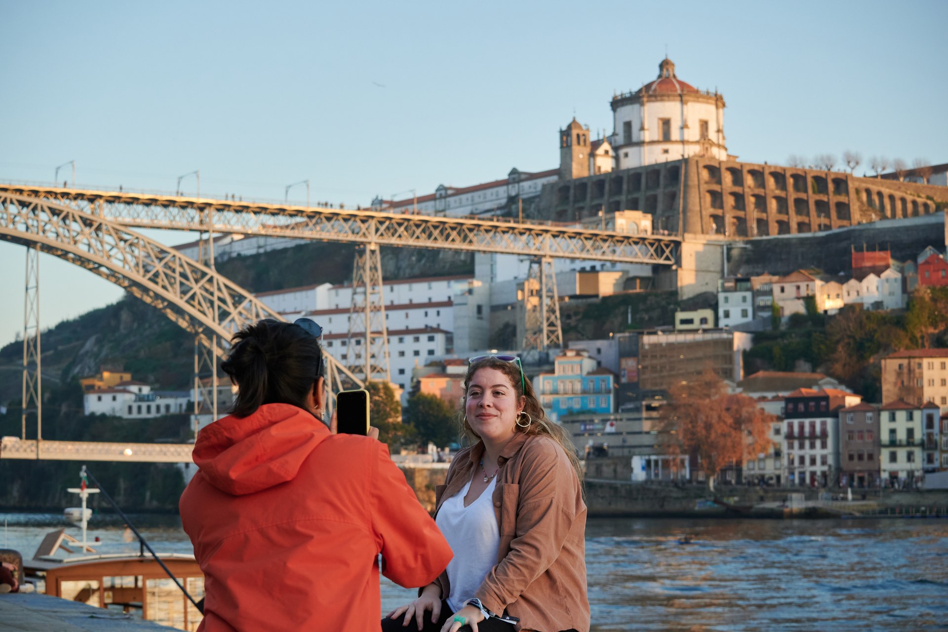 Młoda kobieta fotografuje przyjaciółkę na tle mostu w Porto