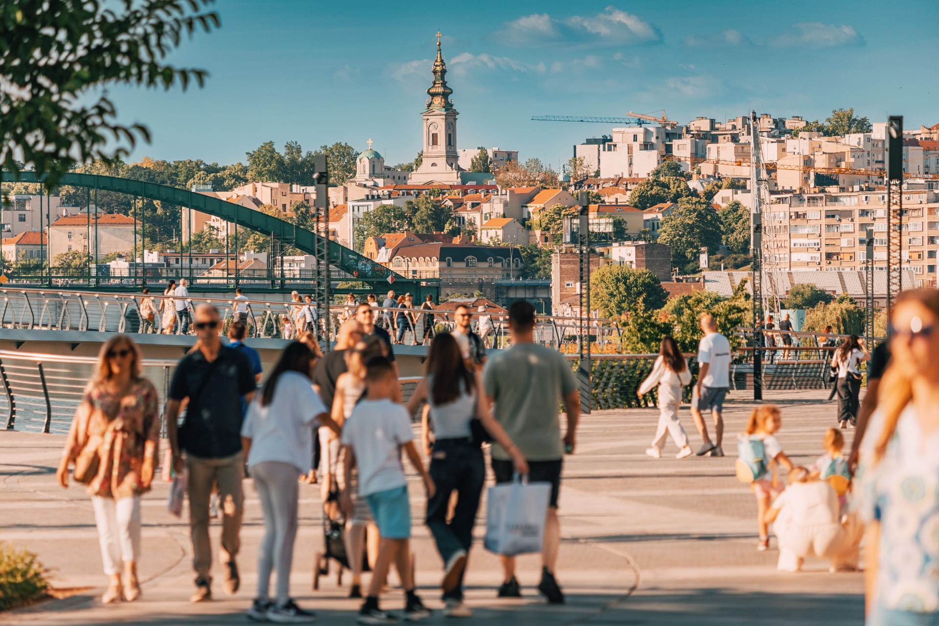 Spacerowicze na promenadzie nad Sawą w Belgradzie, w tle stare miasto i wieża kościoła