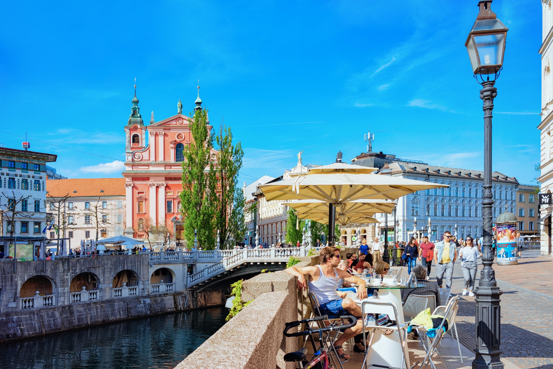 Ludzie przy stolikach kawiarni na Potrójnym Moście nad Lublanicą w Lublanie